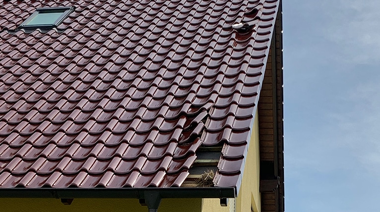 Ein Dach mit einem Sturmschaden bei dem die Ziegel verrutscht sind von unten fotografiert.