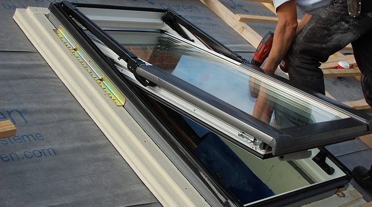 Ein halb aufgekipptes Dachfenster, das von einem Dachdecker gerade eingebaut wird